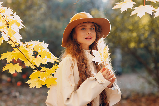 Smiling young woman portrait in the autumn forest with the yellow leaves at sunset