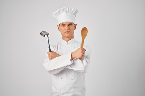 a man in a chef's uniform with a ladle in his hands preparing food light background. High quality photo