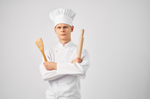 male chef with a cap on his head and kitchenware light background. High quality photo
