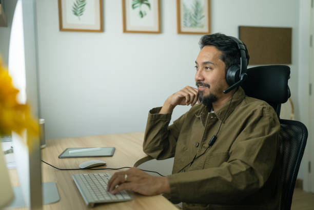 istock Asian man with headset having video call on  computer in his home office 2079519365