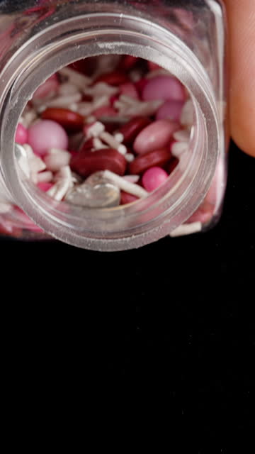 Vertical video. In Pink Tones, Sweet Decorations in the Form of Hearts and Balls Pour Out from a Jar.