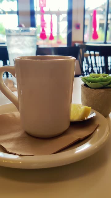 Steaming tea of coffee mug hot beverage with a slice of lemon on a restaurant table vertical 4k video. Morning relaxing moment. Breakfast. Healthy drink.