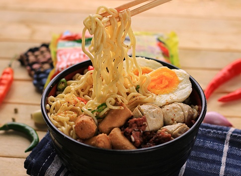 Boiled noodles containing eggs, sausages, meatballs, corned beef, chilies are served in a bowl