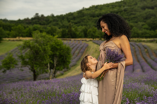 A Latina woman with her daughter holds a bunch of lavender in the middle of a lavender field at sunset. Mom holds light lanterns in her hand.