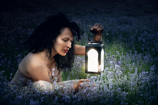 Latino, afro-american woman in the dark of the night with her daughter in a lavender field at night examines lavender flowers and holds light lanterns in her hand