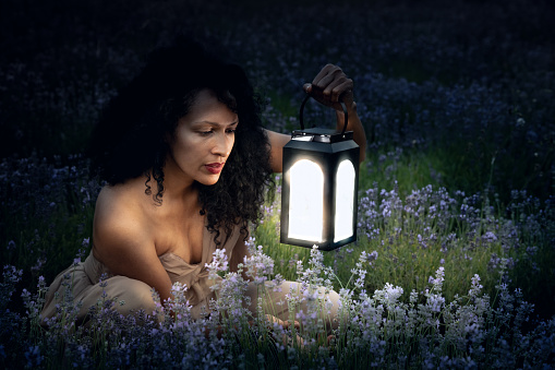 Latino, afro-american woman in the dark of the night with her daughter in a lavender field at night examines lavender flowers and holds light lanterns in her hand