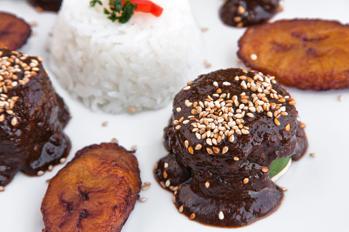 Mexican mole, chicken rolls with Mexican mole, sesame, rice and fried plantain on white background