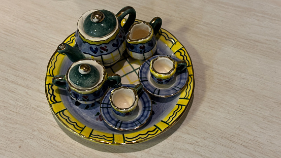 A collection of small teacups and a teapot are displayed on a table. The teapot is green and the cups are white. The table is surrounded by other items, including a vase and a bowl