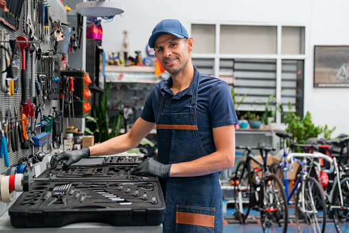 Latin American mechanic using tools while working at a bicycle repair shop and looking at the camera smiling