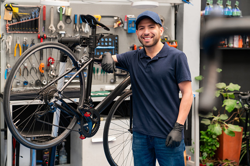 Happy mechanic fixing a bicycle at a repair shop and looking at the camera smiling