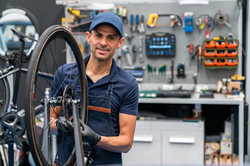 Portrait of a Latin American mechanic fixing a flat tire on a bicycle at a repair shop and looking at the camera smiling