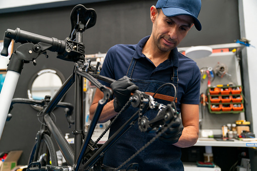 Portrait of a Latin American mechanic fixing a bicycle at the repair shop and looking at the camera smiling