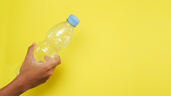 Hand holding plastic bottle from PET Polyethylene Terephthalate material on yellow background