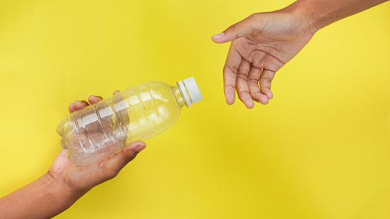 hand giving plastic bottle from PET Polyethylene Terephthalate material and receiving on yellow background