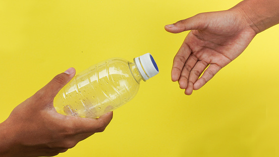 hand giving plastic bottle from PET Polyethylene Terephthalate material and receiving on yellow background