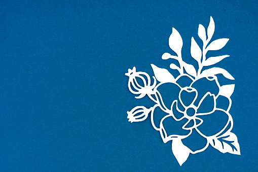 Carve of white paper flower and leaves with copy space on a blue cardboard background.