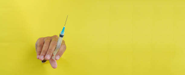 istock Hand holding disposable plastic syringe on yellow background 2079749979