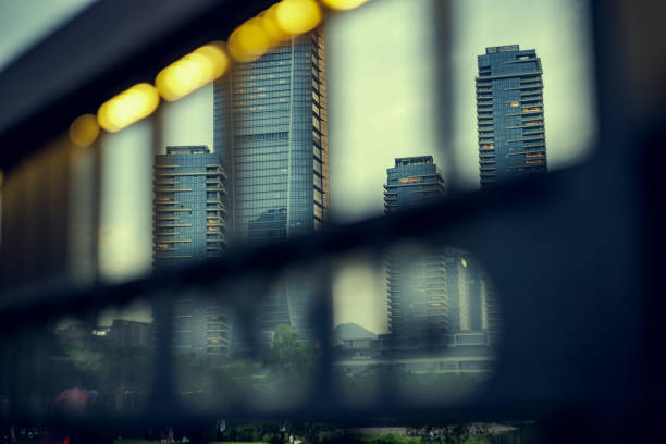 An obscured view through metal grates offers a glimpse of towering buildings, mingling urban elements with soft light.