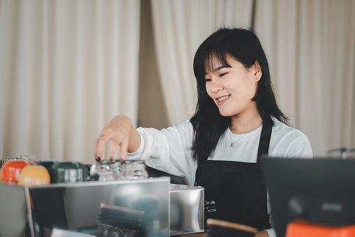 A smiling barista in a black apron arranges cups at a coffee shop, her pleasant demeanor adding warmth to the ambiance.
