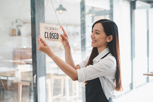 A cafe owner displays a 'Sorry We Are Closed' sign with a content smile, marking the end of a fulfilling day of business in her welcoming establishment.