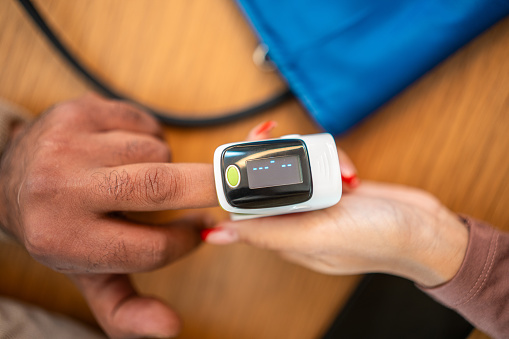 A close-up shot showing the hands of a diverse female and male, one wearing a pulse oximeter. They are indoors, with emphasis on health monitoring, using medical technology for checking vital signs.