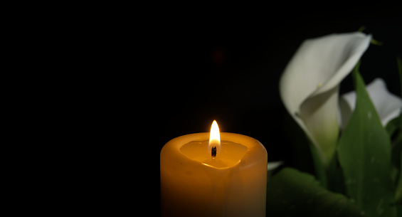 White calla lily flower next to glowing candle flame casts a warm light in a dark environment and creates a soothing ambiance, radiating a sense of peaceful solitude