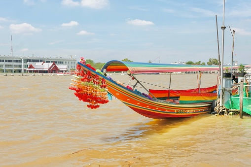 A colourful Thai longtail boat with flower garlands docked on the banks of the Chao Phraya River near Tha Tien Pier (across Wat Arun) — Phra Nakhon, Bangkok, Thailand