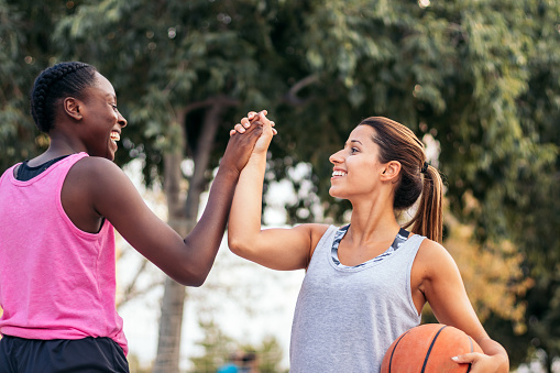 Young female athletes playing basketball in sportswear on an urban court in the city. They have fun and high five enjoying the sport.
