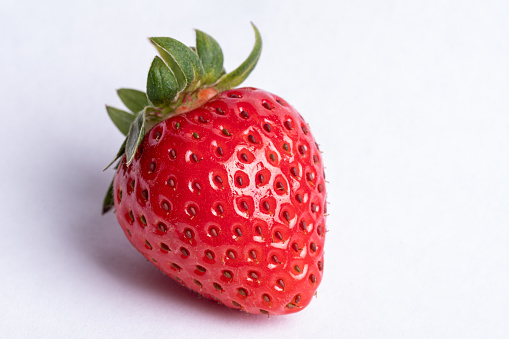 Close up view of strawberry plant, leaves, bloom and fruit on white background.