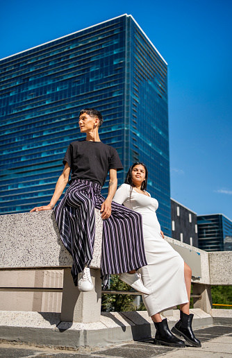 Two young models wearing stylish outfits posing with attitude together outside in the city in summer