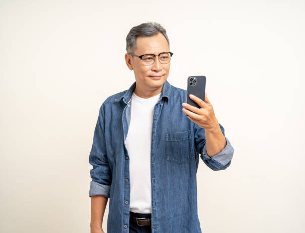 istock Handsome asian mature old man standing using smartphone on isolated white background. Happy Portrait of cheerful smiling senior asian man holding cell phone. Mature People and lifestyle 2079944972