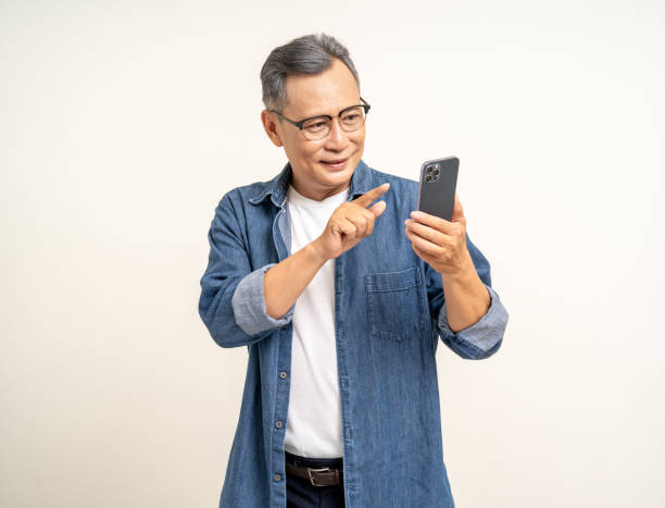 istock Handsome asian mature old man standing using smartphone on isolated white background. Happy Portrait of cheerful smiling senior asian man holding cell phone. Mature People and lifestyle 2079951172