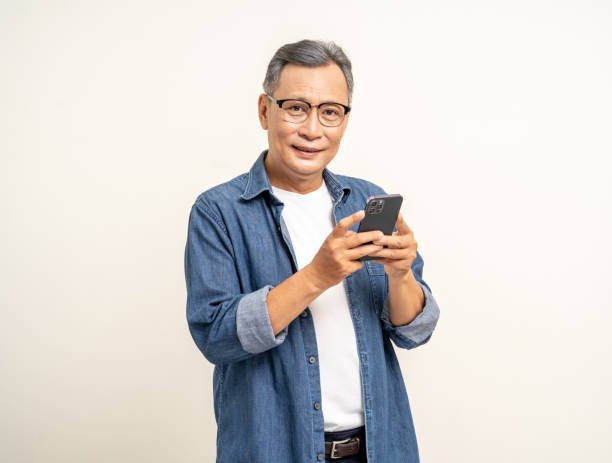 istock Handsome asian mature old man standing using smartphone on isolated white background. Happy Portrait of cheerful smiling senior asian man holding cell phone. Mature People and lifestyle 2079967278