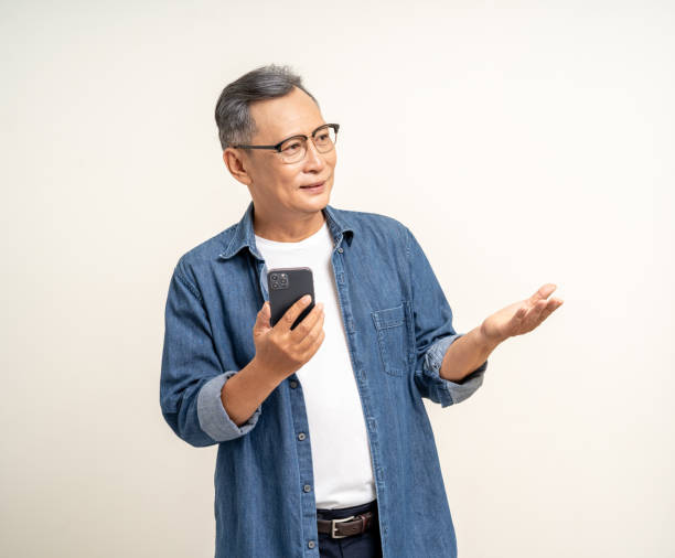 istock Handsome asian mature old man using smartphone palm up  pointing hand on copy space isolated white background. Portrait of cheerful smiling senior asian man holding cell phone. Mature People and lifestyle 2079975043