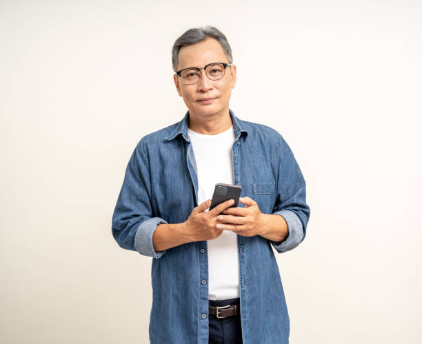 istock Handsome asian mature old man standing using smartphone on isolated white background. Happy Portrait of cheerful smiling senior asian man holding cell phone. Mature People and lifestyle 2079982316