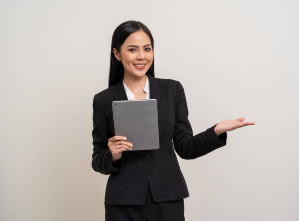 istock Attractive elegant young asian business woman using digital tablet standing on isolated background. Happy young latin female formal black suit holding tablet gadget working service with customer 2079986920