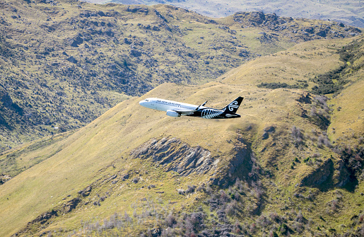 Queenstown, New Zealand - 30 Dec 2023. Air New Zealand jet gaining altitude with lush green mountains in the background.