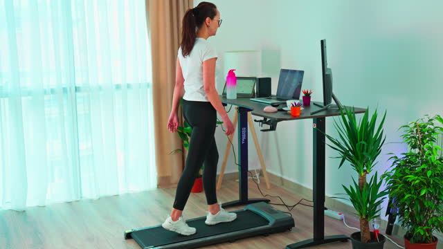 Woman at home office is walking on under desk treadmill
