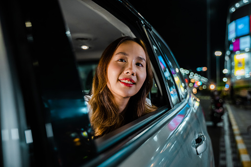 A woman enjoying a scenic car ride, looking out of the window at the night street scenery. The journey is an escape from the business of everyday life.