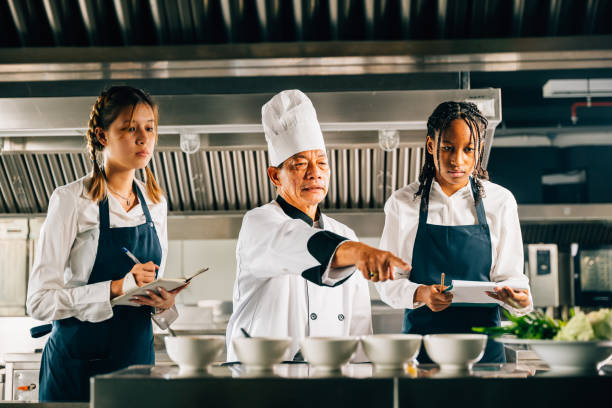 istock Professional Asian senior chef guides diverse students in a restaurant kitchen. Focusing on teamwork learning and note-taking in this educational workshop. Food Edocation 2080039121