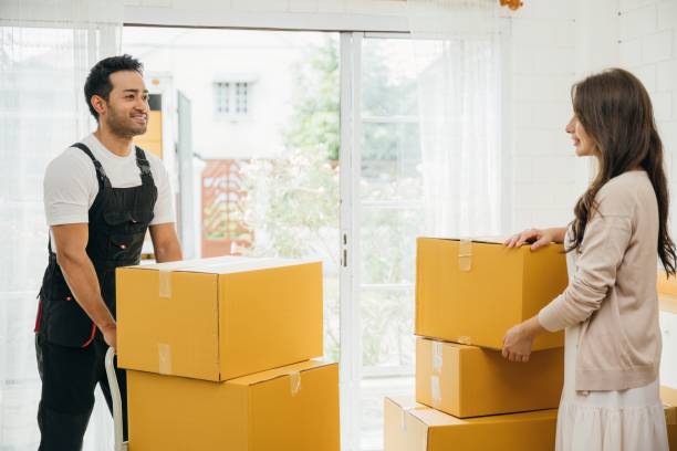 istock Movers in uniform assist couple indoors unloading boxes from truck. Professional service guarantees customer satisfaction during relocation. Efficient teamwork and assistance portrayed. Moving day 2080044905
