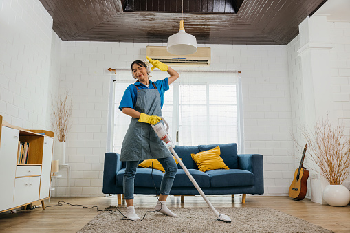 Asian housewife's fun cleaning, singing dancing with mop microphone. Joyful occupation filled with music laughter. Modern housework enjoyment. Give me a rhythm, maid dancing having fun