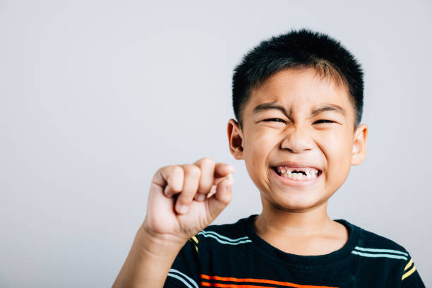 Um menino segura um dente de leite caído significando higiene bucal. O primeiro dente perdido incorpora o desenvolvimento da criança, a alegria e o crescimento. Crianças apresentam nova lacuna nos dentes, problemas com dentistas - foto de acervo