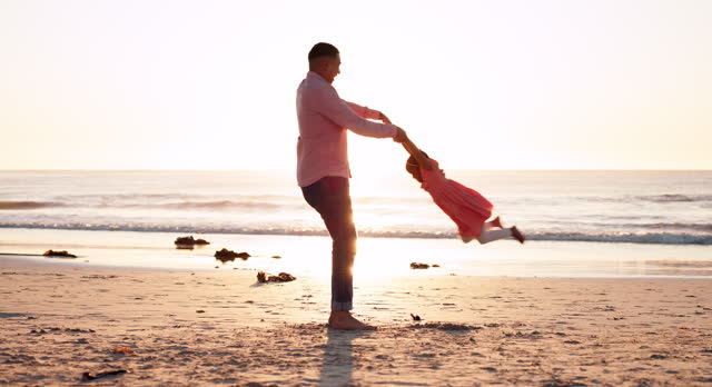 Family, beach and a man spinning his daughter at sunset while bonding together during summer vacation. Kids, freedom or travel fun and a father playing with his girl child on the sand by the ocean