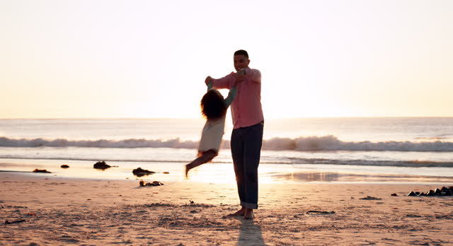 Family, beach and a father spinning his daughter at sunset while bonding together during summer vacation. Kids, freedom or travel fun and a man playing with his girl child on the sand by the ocean