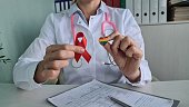 Doctor holding LGBT badge and red ribbon. HIV AIDS and the health of sexual minorities