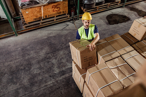 High angle view of young manual worker working with carton boxes in a distribution warehouse. Copy space.