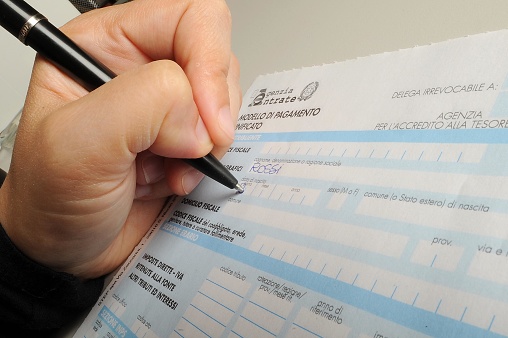 Filling out forms to pay taxes in Italy. The forms are called F24 and recognized as proxies. Pictured is a person writing and filling out forms for contributions.