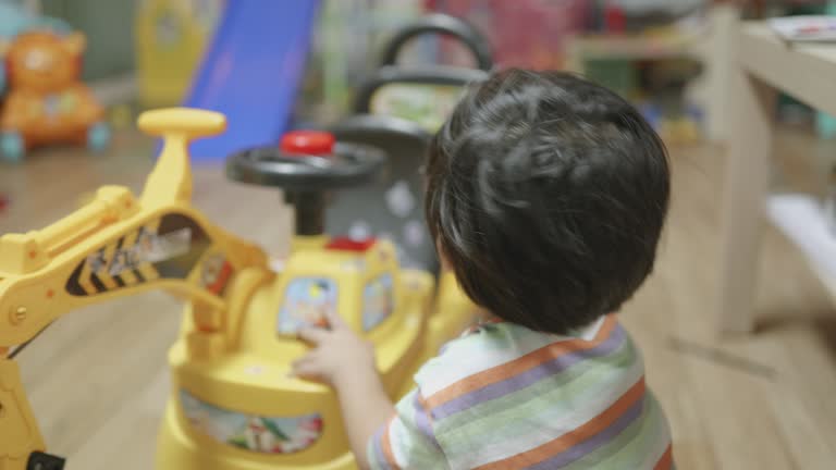 Happy Asian boy playing with toy backhoe in the living room at home. Drive to repairs with imagination.