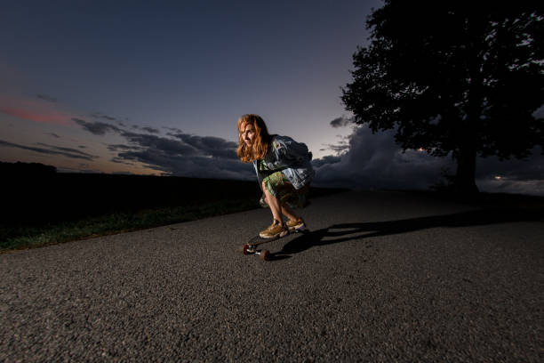 istock Young girl riding a longboard on the road, looking ahead in concentration 2080211852